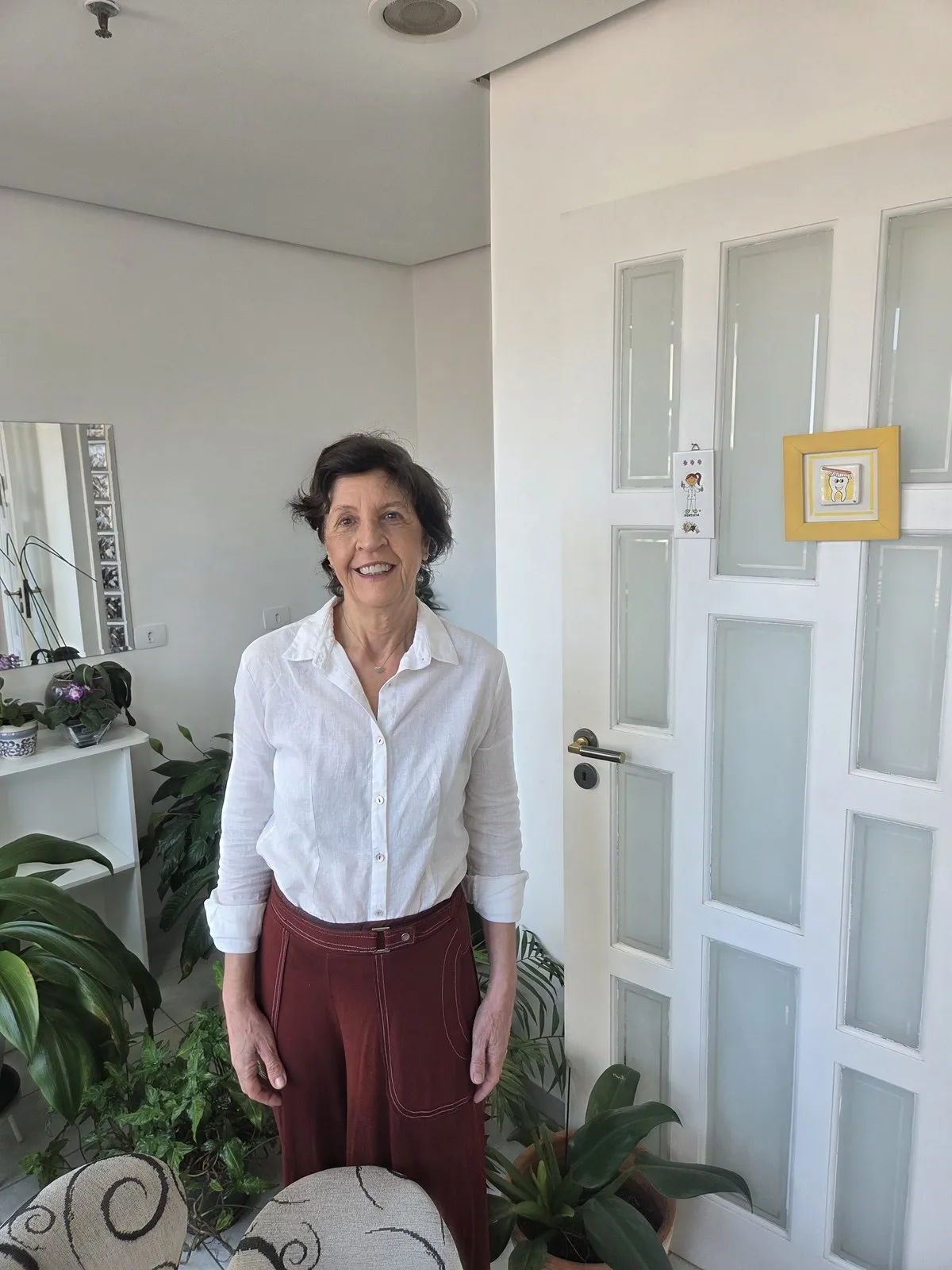 Retrato de Ana Junqueira, de meio corpo, com o ambiente do consultório ao fundo.